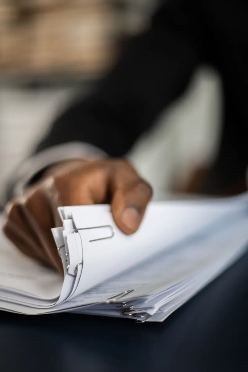 Close-up of a hand leafing through a thick stack of paper-clipped documents