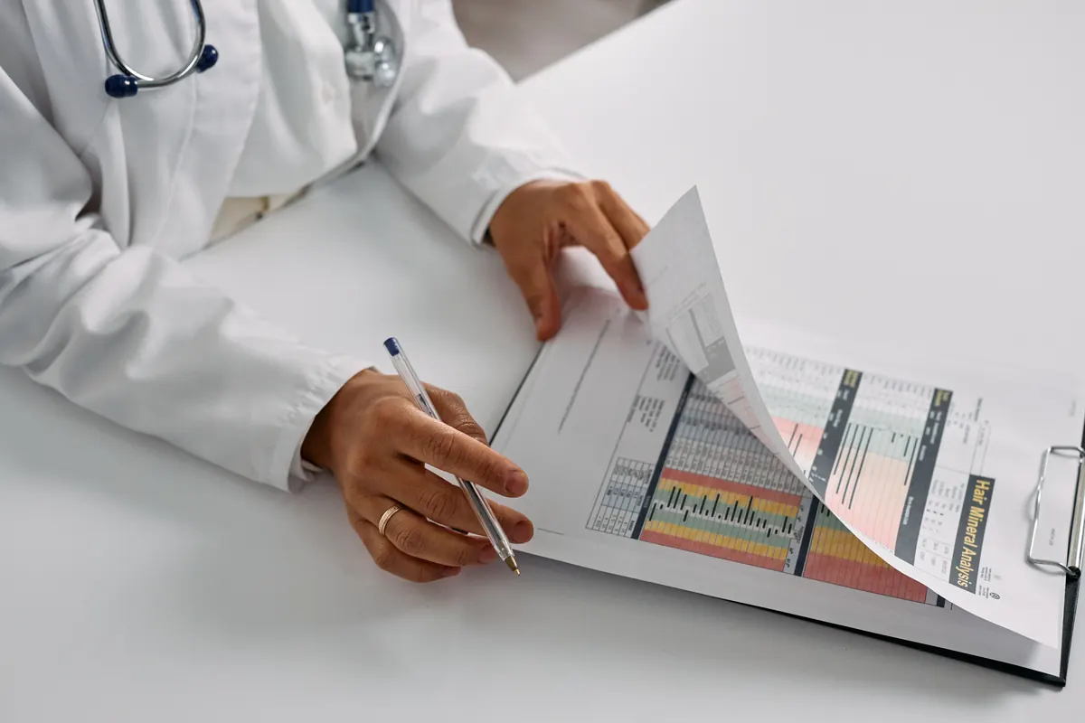 A doctor in a white coat with a stethoscope turning the pages of a color-coded report on a clipboard