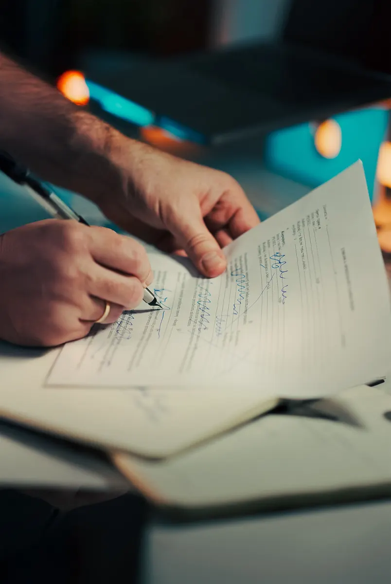 Close-up of a man's hands signing a printed form with a pen in warm evening light