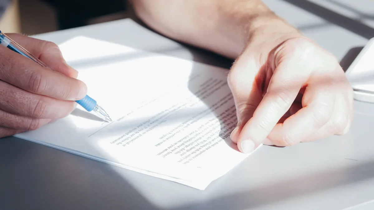 Close-up of hands writing on a printed letter with a blue pen in bright sunlight