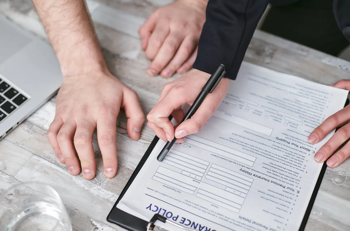 One person pointing with a pen at an insurance form on a clipboard while another person looks on