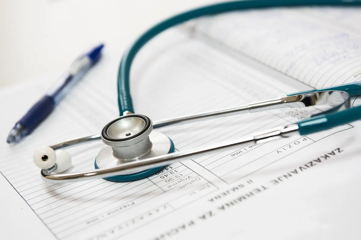 Close-up of a teal stethoscope and a blue pen resting on a printed appointment sheet