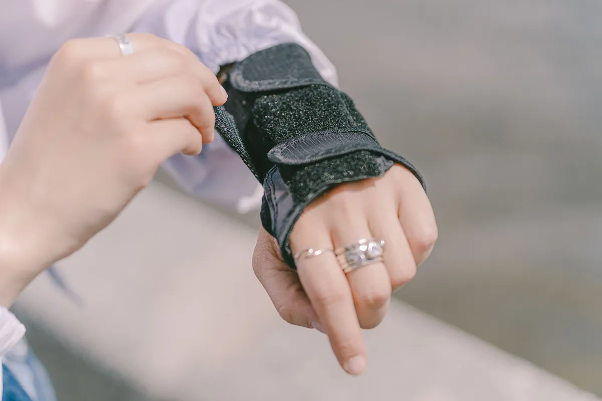 Close-up of a woman fastening a black brace around her wrist and hand