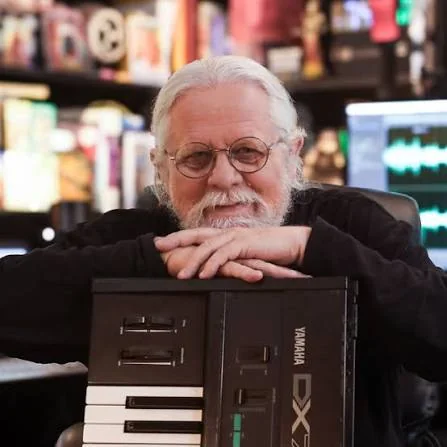 Dr. Jeffrey Thompson in his studio, resting his arms on a synthesizer